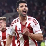 Οι παίκτες του Ολυμπιακού πανηγυρίζουν σε ευρωπαϊκό αγώνα, με φόντο τη μάχη για το Champions League.